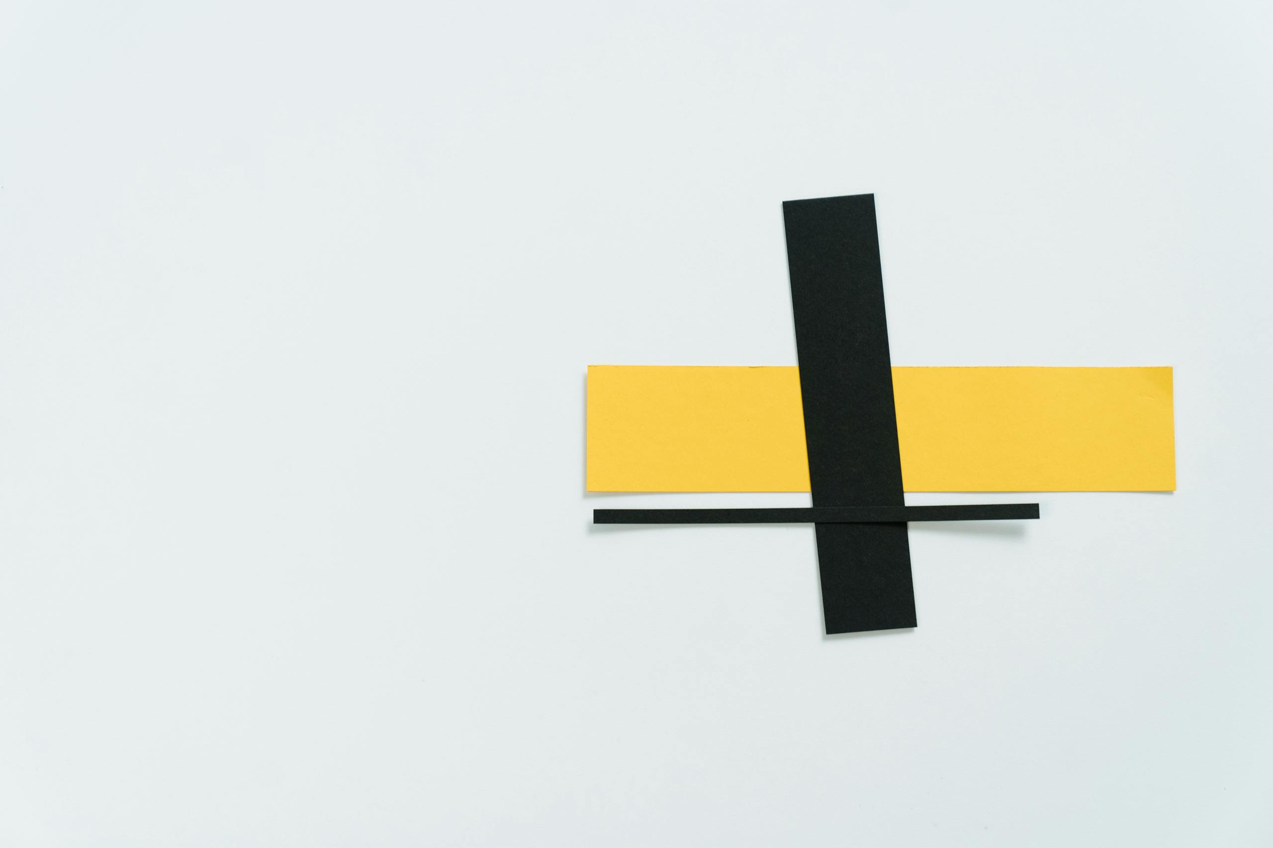 A minimalist composition featuring intersecting black and yellow paper strips on a white background.